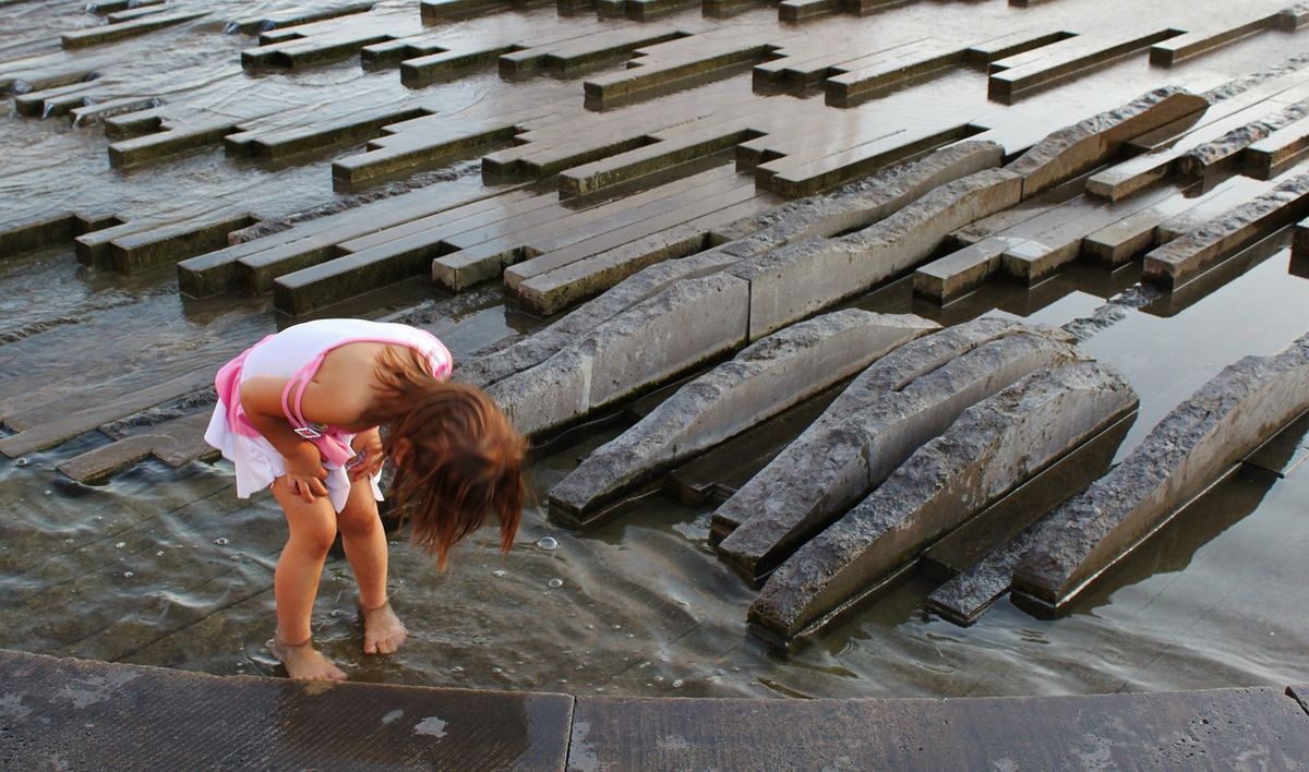 A small child playing barefoot in a shallow water feature on a city square